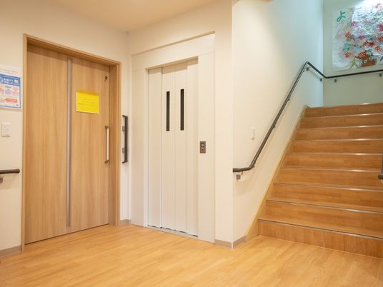 階段の横の白い壁に配置された白い扉が閉まったエレベーター