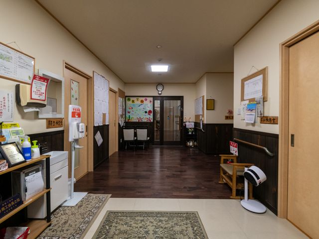 廊下に掲示物と椅子 玄関 案内掲示が豊富な快適な通路は、訪れる皆さまに分かりやすい情報提供を心がけております。スタッフや利用者様の気配が感じられる温かい空間です。