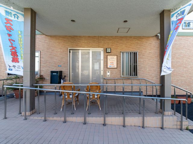 施設前の屋根付き玄関 エントランス   屋根付きの玄関前には手すり付きのスロープがあり、出入りしやすいつくりです。前面は開放感があり、来訪者を迎える落ち着いた雰囲気です。