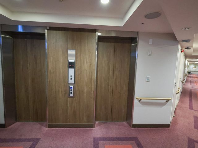 二台の縦型移動装置と廊下 エレベーター 広々とした廊下にはエレベーターが二台設置され、安全に移動ができる環境です。
