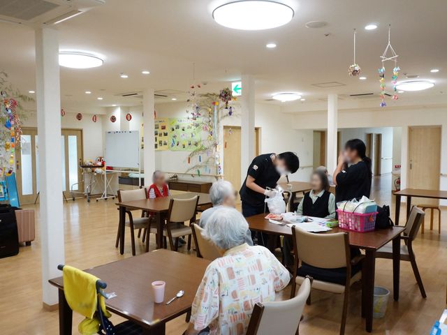 共有スペースの活動風景 談話室 スタッフが利用者様のそばで気配りをもって支援しており、憩いの時間を過ごしている様子が伺えます。明るく開放感のあるダイニングでのふれあいを提供しています。