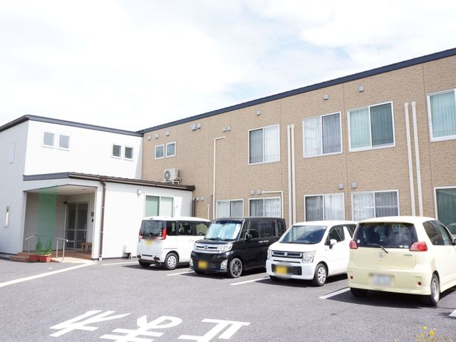 施設の駐車場とエントランス 外観 快晴の日差しのもと、清潔感のあふれるエントランスがお出迎えします。広々とした駐車スペースがあり、来訪もスムーズです。