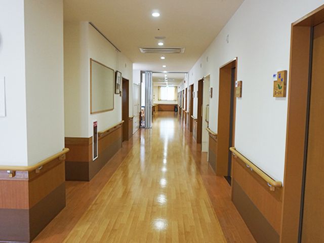 長い廊下の様子 廊下 暖かい木目調の通路が、落ち着いた雰囲気を作り出しています。奥には光が差し込んでいます。