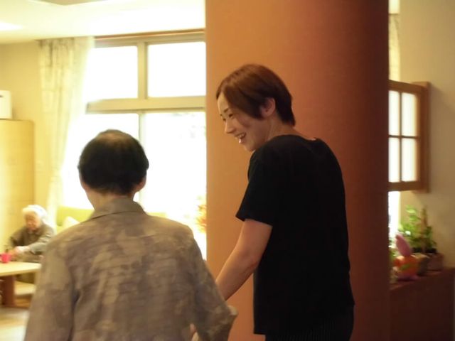 笑顔で支援するスタッフ リビング 笑顔で手を取り合い、向かい合う方々の姿が温かい雰囲気を醸し出しています。安心のサポートをお感じいただけます。
