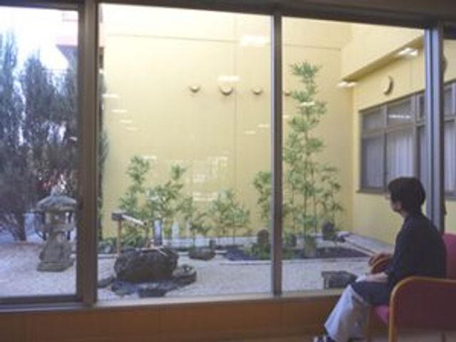 中庭を見る人 中庭 ゆったりとした椅子に座り、緑豊かな中庭の景色をお楽しみいただける空間です。癒やしの時を提供いたします。