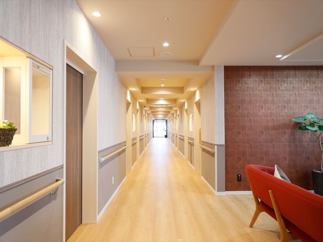 明るい廊下の風景 廊下 手すりが設置された、ゆったりとした通路は、歩行に不安のある方でも安心してお使いいただける設計になっています。木目調のフロアが温もりを感じさせ、気持ちを落ち着かせてくれます。