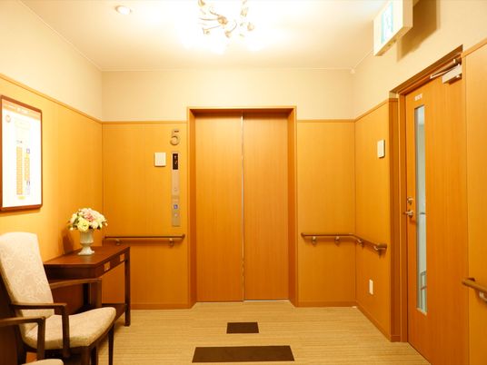 エレベーターの前に椅子があり、待つ間に座っていることができる。壁面の手すりは、扉まで続いて取りつけてあるので安全に移動できる。