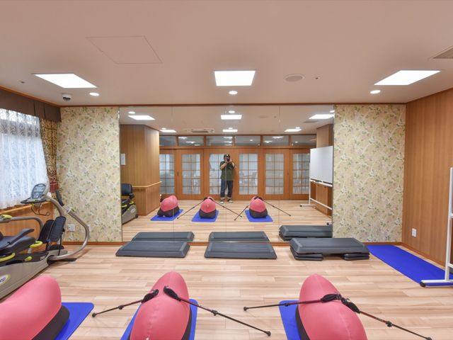 多彩な運動器具の機能訓練室 トレーニング室 整えられた機能訓練室で、明るく清潔な環境の中、自らの体を鍛える方が映っています。ケアを提供する側も積極的なご利用をサポートできる設備が整っています。