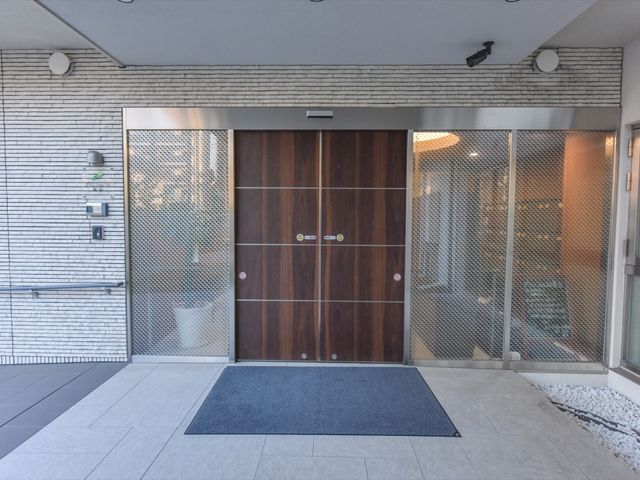 木目調のエントランス扉 玄関 手入れの行き届いた明るいエントランスで、来訪者を温かく迎えます。安心し、憩いの時を過ごす場所です。