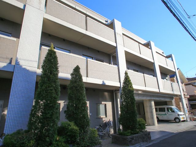 多層建築の外観 屋根 多階層の建物が立つ明るい外観です。入口付近には、送り迎え用の車が停まっており、利便性が確保されています。