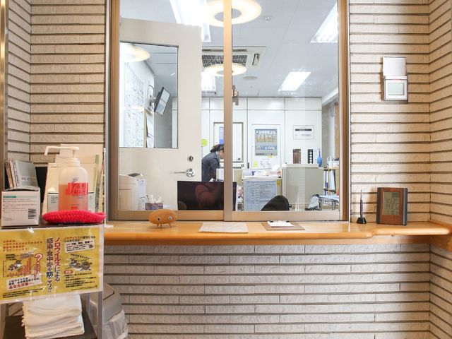 窓越しのフロント風景 受付 清潔で開放感のある受付エリアです。スタッフの方が丁寧に対応される様子が伺えます。