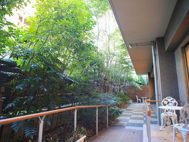 中庭の緑溢れる通路 テラス 植栽に囲まれた通路は、散策や憩いの時間に心地よい空間を提供します。白い椅子が設置され、リラックスできる場所となっています。