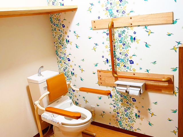 バリアフリートイレ 手すり付きで明るい花柄の壁が印象的なトイレです。安全かつ快適にご利用いただけるよう配慮されています。