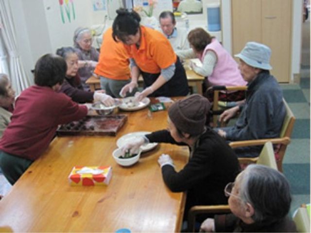 調理活動する利用者と職員 日常 笑顔あふれる活動風景です。利用者とスタッフが手を取り合いながら、共に調理の時間を楽しんでいます。