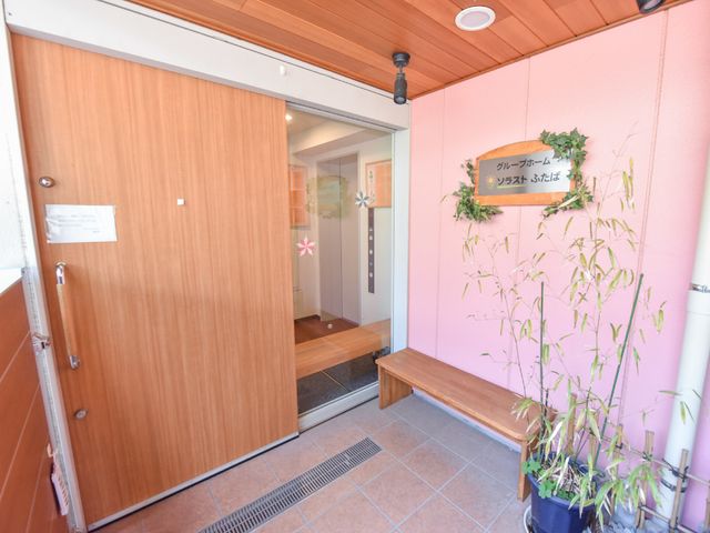 温かみのあるエントランス 玄関 心地よい木製の扉を備えた入り口は、来訪者を暖かく迎えます。植物の飾りつけが空間に柔らかな雰囲気を加えています。
