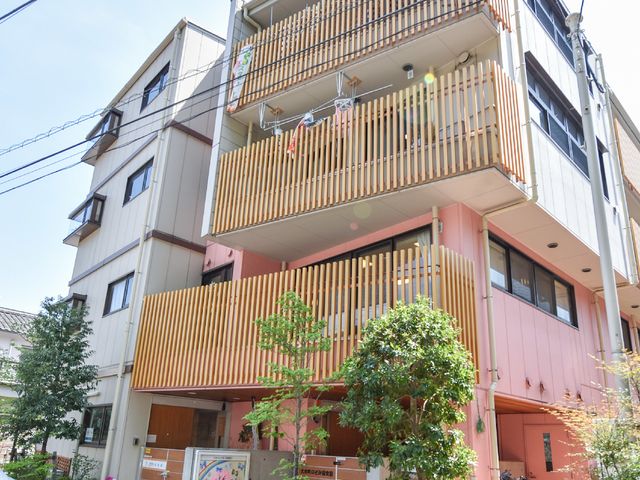 ピンク外壁の建物正面 外観 洗練されたデザインの外壁が目を引く建物です。明るい色合いが、訪れる方々を暖かくお迎えします。