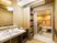 大きな鏡付の洗面台や脱衣かご棚のある脱衣所の奥に、壁に手すりがたくさんついた浴室がある。入浴用の介護機器も置かれている。