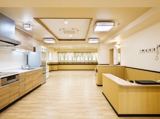 施設の写真 腰板の木材が優しい雰囲気を作りだす、広い空間。食器棚や大型の冷蔵庫、システムキッチンが設置されている。