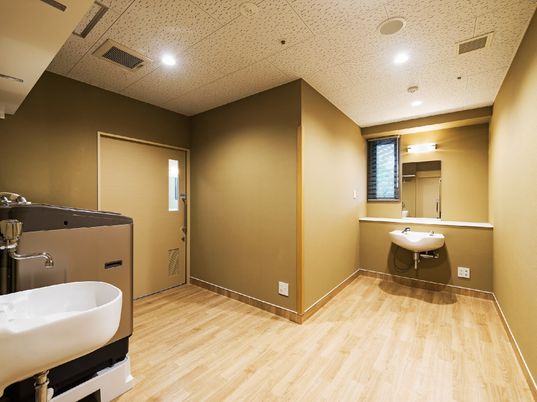 施設の写真 ベージュ系の落ち着いた色調の室内には、片側にシャワー付きの洗髪台、もう一方には大型の洗濯機やシンクが設置されている。
