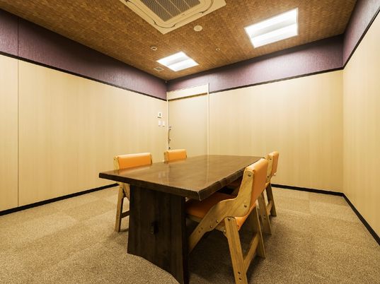 組み木細工調の天井が美しい部屋である。中央に、木目がしっかりと見える濃い茶色のテーブルと、椅子が４脚置かれている。