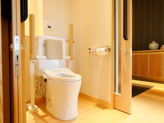 居室のトイレは引き戸で仕切られた個室で、床には段差がない。温水洗浄便座がついており、背もたれと肱掛けもある。
