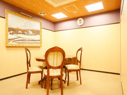 施設の写真 アンティーク調デザインの椅子とテーブルが、リビングの真ん中あたりに置いてある。左側の壁には、大きな絵が掛けてある。