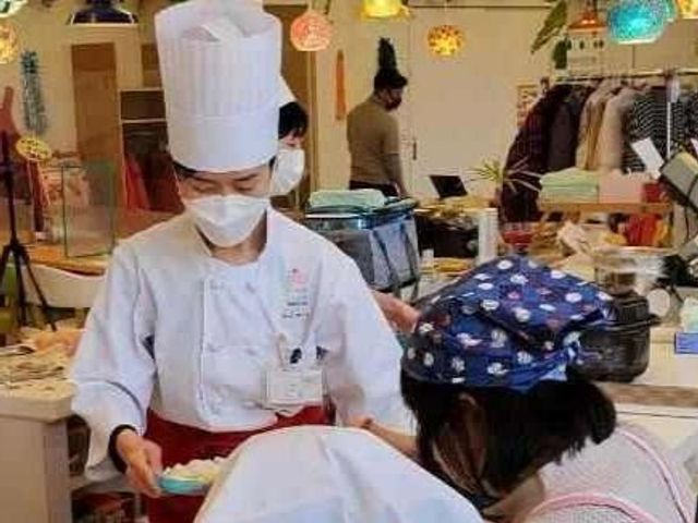 料理を学ぶ人々の様子 多目的室 利用者が料理の技術を楽しく学ぶ光景です。笑顔で指導するスタッフの姿が見られます。