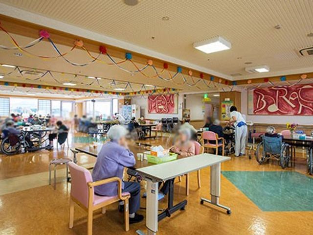 明るい広い部屋 ダイニングルーム 広々とした明るい空間で、利用者の方々がリラックスして過ごしています。飾り付けが華やかです。