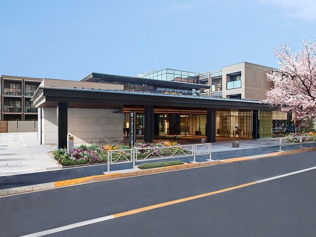 施設外観 外観   落ち着いた色合いの建物に、花壇と桜が彩りを添えています。車寄せも見え、送迎時の動線が想像しやすい外観です。