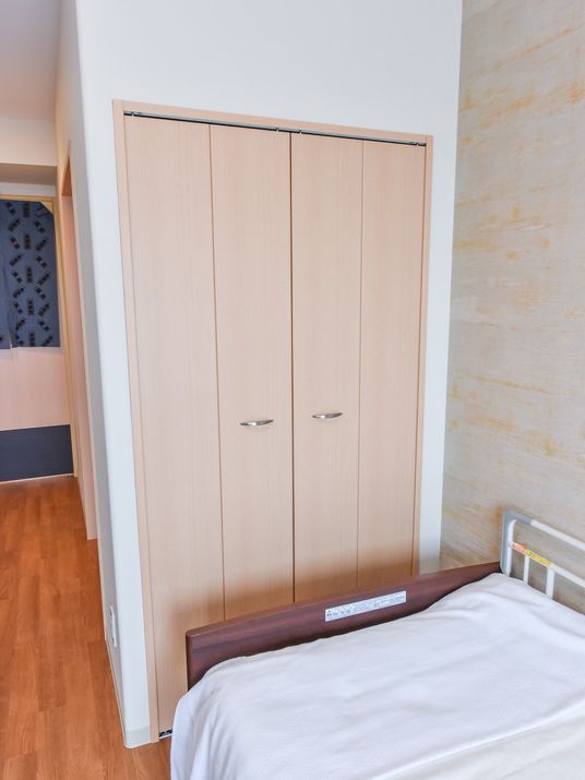 部屋の壁際にベッドが置かれている。ベッドのそばには、埋め込み型の両開きのクローゼットが設置されている。