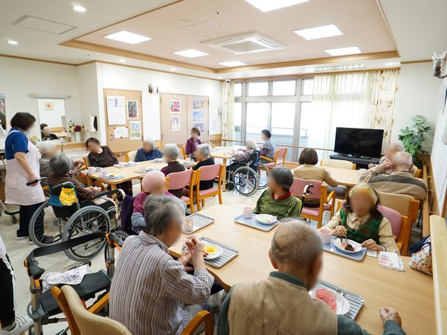 共有スペースでの食事風景 食堂 暖かい雰囲気の食堂で、利用者が心地よく食事をしています。スタッフの方々も優しくサポートしており、何かと温かなコミュニケーションが見られます。