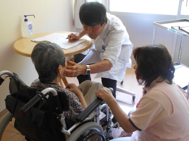 笑顔で話すスタッフと利用者 機能訓練室 スタッフが丁寧にサポートする機能訓練の様子。車椅子の方も安心して日々の訓練に取り組める環境です。