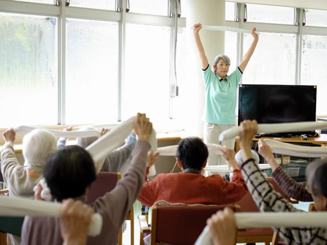 運動中のエクササイズルーム 機能訓練室 スタッフの指導のもと、利用者の皆さまが体操を行っている様子です。明るい雰囲気の中で健康維持に努めています。