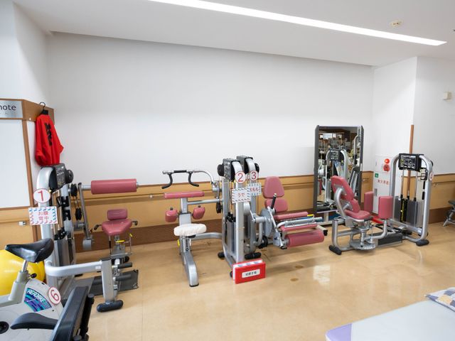 リハビリ機器が並ぶ部屋 機能訓練室 整った設備で日々のリハビリを支えます。テーブルや鏡も備え、明るく清潔な空間です。