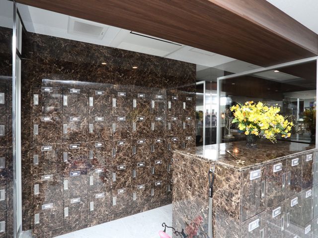 フロントの花と郵便受け 玄関 光沢のある大理石調のカウンターに生花が華やかな印象を与えており、来訪者を温かく迎える空間が整っています。