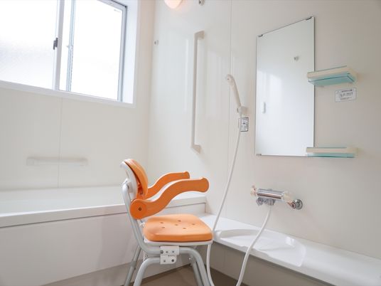 個浴用浴室には介護用椅子が１脚置かれている。壁に手すりが設置されており、流し台の鏡の横には小型の収納が取り付けられている。