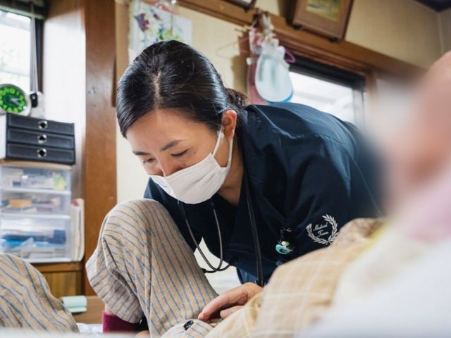 人と交流する看護師 居室 明るい居室で、親身になって入居者と会話するスタッフの姿が印象的です。