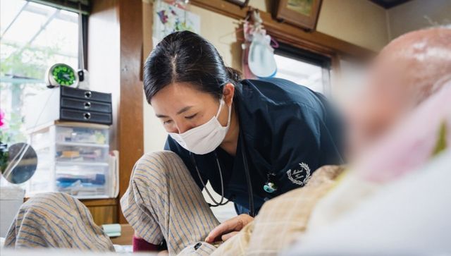 人と交流する看護師 居室 明るい居室で、親身になって入居者と会話するスタッフの姿が印象的です。