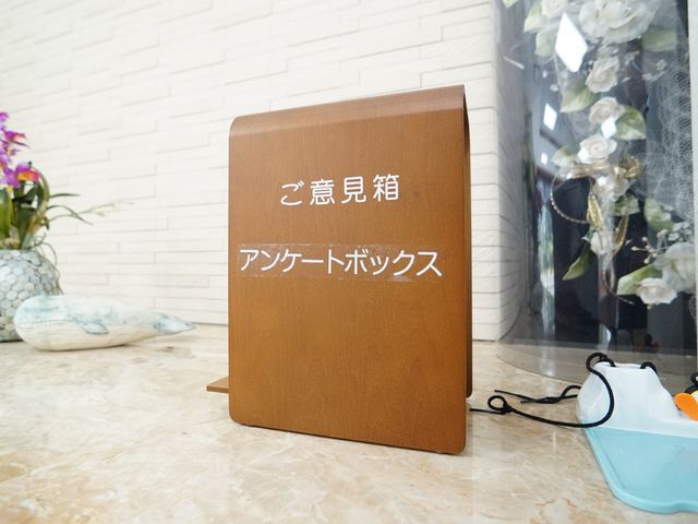 案内看板のクローズアップ アンケートボックス 清潔感あふれる入り口には、温かみのある案内看板が設置されており、優雅な印象を受ける空間が広がっています。