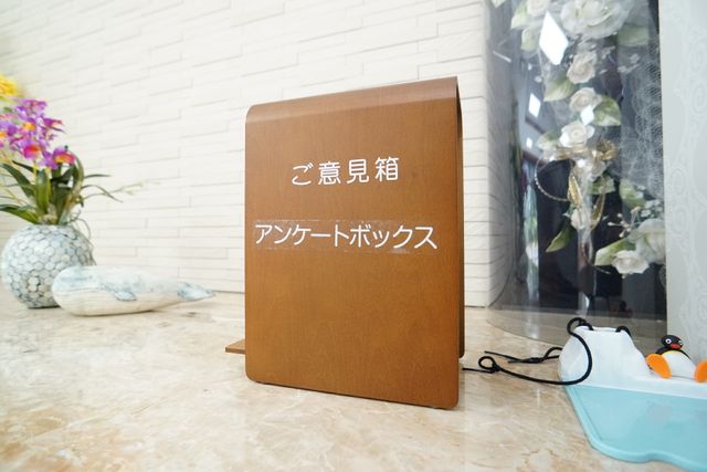案内看板のクローズアップ アンケートボックス 清潔感あふれる入り口には、温かみのある案内看板が設置されており、優雅な印象を受ける空間が広がっています。