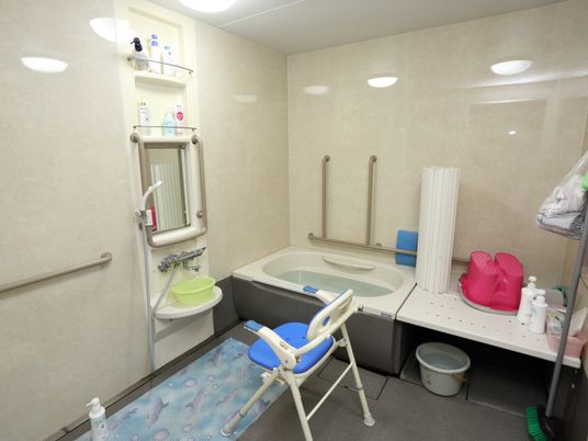 施設の写真 浴室内は広くなっている。壁には用途に合わせた向きの手すりがつけられ、シャワーの下にはマットが敷かれている。