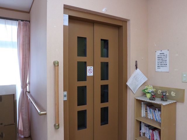 エレベーター入口 本棚 柔らかい色合いの壁が特徴的なエレベーター入口です。手すりが付いており、どなたでも安全にご利用いただけます。