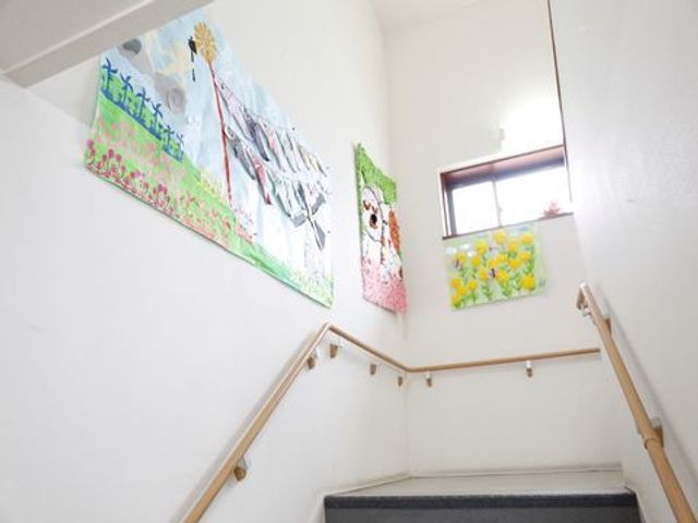 階段と絵画のある廊下 階段掲示物 階段の壁面にはカラフルな絵画を飾り、温かみのある雰囲気を演出しています。明るく清潔感のある通路を保っており、快適にお過ごしいただけます。