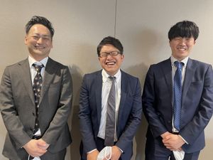 笑顔の男性3人が並ぶ会議室  