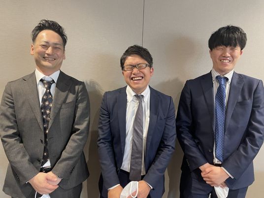 笑顔の男性3人が並ぶ会議室  