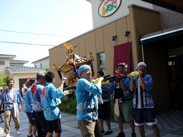 祭り気分を楽しむ人々 北四ツ居神輿 青い法被を着た笑顔のスタッフが、地域のお祭りを再現するイベントで盛り上がっています。地域文化を大切にし、楽しい雰囲気作りに努めている様子が伝わります。