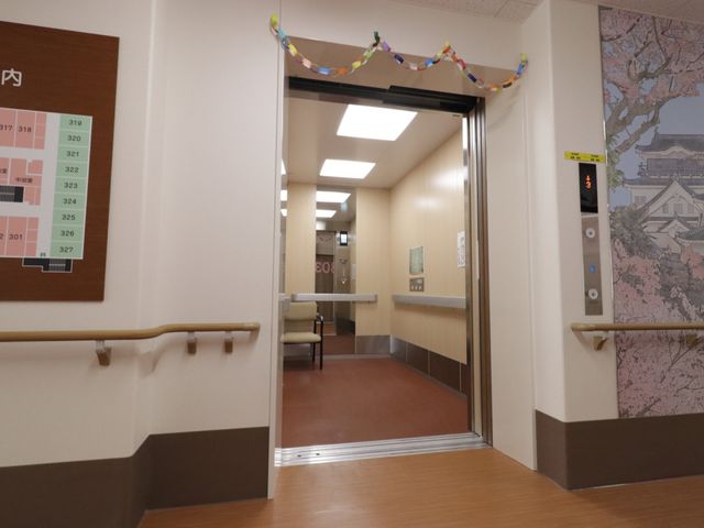 廊下に面した自動ドア エレベーター 広々とした廊下は清潔感があり、壁には掲示物も配され、訪れる方々への温かなおもてなしが感じられます。