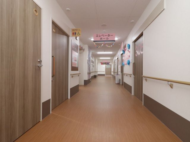 清潔な廊下 廊下 手すりが設置された清潔でゆったりとした通路です。壁には掲示物や装飾があり、明るい雰囲気が演出されています。