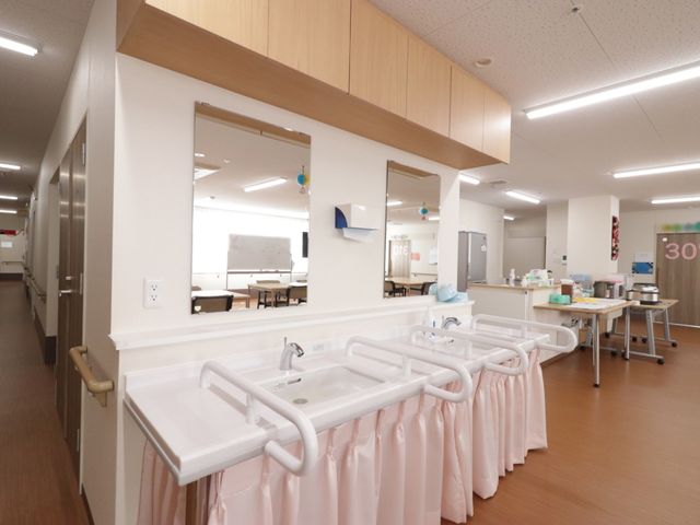 洗面台と見える共用スペース 洗面台 広々とした洗面スペースがあり、清潔感のあふれる環境で日々のケアをサポートします。手すりも設置されており、安心してご利用いただけます。