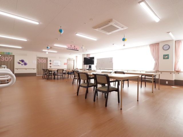 広々とした多目的スペース 食堂 ゆったりとした空間で、日常の様々なアクティビティが行える多目的室です。テーブルと椅子が配置され、明るく開放感のある環境が整っています。
